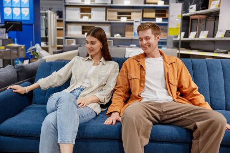 Téléchargez les photos : Couple homme et femme détendu assis sur un canapé testant le confort des meubles. Shopping au showroom d'ameublement - en image libre de droit