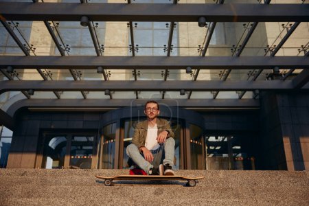 Téléchargez les photos : Cool étudiant gars avec longboard repos sur les escaliers de l'université bâtiment urbain. Skateboard comme moyen de transport en ville - en image libre de droit