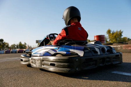 Photo for Back view shot of competitive racer driving go-cart sports track outdoors. Car pilot confidently moving fast to finish line - Royalty Free Image
