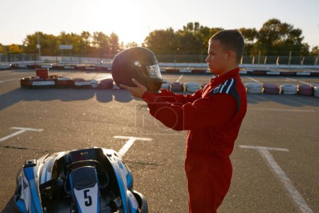 Photo for Young sportsman go-kart driver checking his protective helmet before starting race. Carting training activity, recreational pursuit at sports club - Royalty Free Image