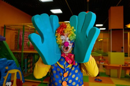Photo for Funny clown with foam hands posing for camera showing happiness and little craziness. Emotional artist wearing colorful wig and costume performing comedian program for kids - Royalty Free Image