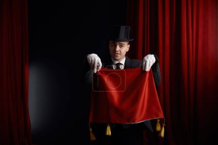 Joven actor mago macho mostrando truco con servilleta en misteriosa atmósfera de teatro escenario con humo. Espectáculo de ilusión y ocupación profesional de personas