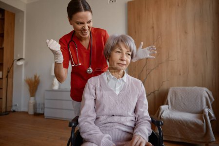 Loca sonriente médico haciendo inyección de tiro para anciana paciente en silla de ruedas cómic foto humorística