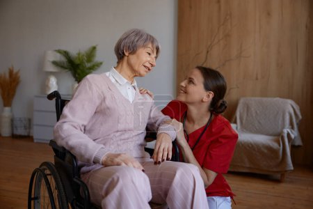 Téléchargez les photos : Portrait d'une femme médecin parlant à sa patiente lors d'une visite à domicile. Femme médecin soutenant et aidant dame âgée en fauteuil roulant. Bonne retraite avec service professionnel - en image libre de droit