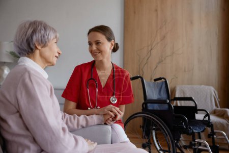 Photo for Female doctor talking to her patient during home visit. Woman medical practitioner supporting and helping elderly lady in wheelchair. Happy retirement with professional service - Royalty Free Image