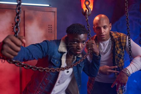 Eine Gruppe moderner cooler Hip-Hop-Tänzer posiert mit Kette und Haken im Garagenstudio. Irrer Rap-Stil und jugendliche Subkultur