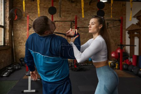 Photo for Young woman performing self-defense move from attacker with knife. Training sparring with instructor at gym - Royalty Free Image