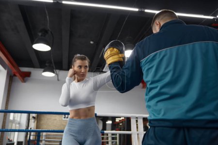 Athletic woman punching to man trainer on taebo training lesson at gym. Sport and female martial arts for self-protection and self-defense concept