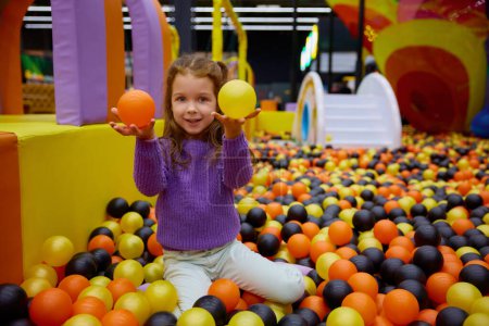 Foto de Retrato de una niña preescolar divertida jugando en el foso de la pelota disfrutando del tiempo feliz activo en el área de entretenimiento para niños. Actividad de ocio y diversión en la sala de juegos - Imagen libre de derechos