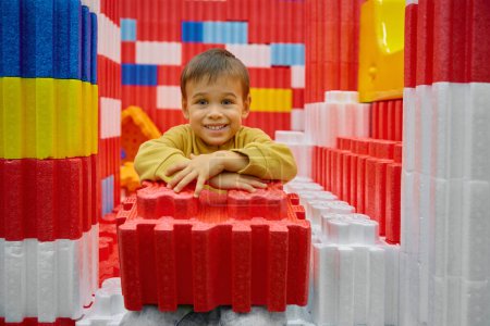 Téléchargez les photos : Garçon enfant jouer avec d'énormes blocs de construction dans le centre de divertissement. Sécurité doux chantier coloré pour les enfants à la garderie aire de jeux - en image libre de droit