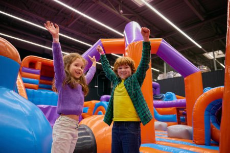 Photo for Portrait of happy excited diverse children with raised hands up enjoying games in inflatable bounce house - Royalty Free Image