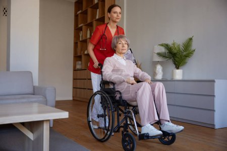 Téléchargez les photos : Femme soignante préparant dame âgée en fauteuil roulant pour la marche. Activités quotidiennes et routinières pour les personnes âgées en maison de retraite - en image libre de droit