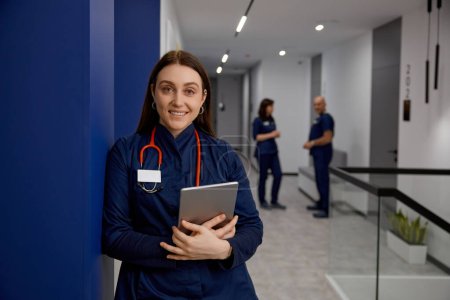 Téléchargez les photos : Portrait de jeune médecin heureux avec tablette numérique dans le couloir de l'hôpital. Concept de gestion d'emploi clinique et de services de santé - en image libre de droit