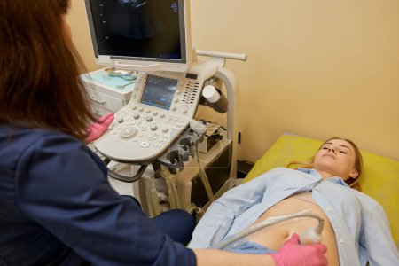 Téléchargez les photos : Gynécologue faisant un test de diagnostic ultrasonique pour le patient avec un équipement moderne au bureau de la clinique. Rendez-vous médical pour l'examen des organes pelviens et la détection précoce de la grossesse - en image libre de droit