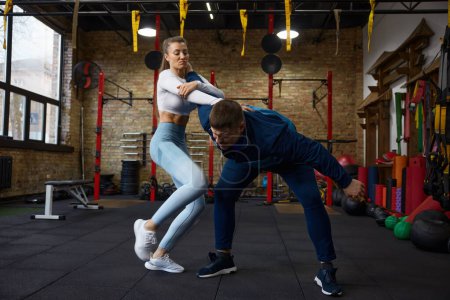Young sportive woman practicing grappling in duel with personal trainer at sport club of martial arts