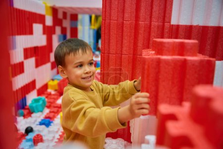 Foto de Niño jugando con enormes bloques de construcción en el centro de entretenimiento. Sitio de construcción colorido suave de la seguridad para los niños en el patio de la guardería - Imagen libre de derechos