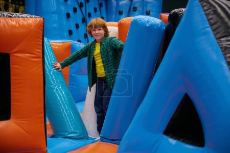 Téléchargez les photos : Enfant garçon actif se sentant excité de jouer dans le château gonflable. Playtime le week-end pour les enfants - en image libre de droit
