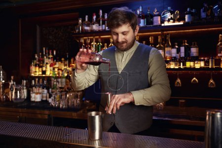 Téléchargez les photos : Barman en uniforme versant la boisson alcoolisée des bouteilles dans shaker en acier derrière le bar - en image libre de droit