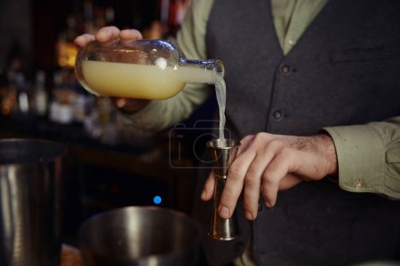 Téléchargez les photos : Gros plan de la main confiant barman mâle boudant liqueur pour faire cocktail debout derrière le comptoir. Service professionnel et concept de profession - en image libre de droit