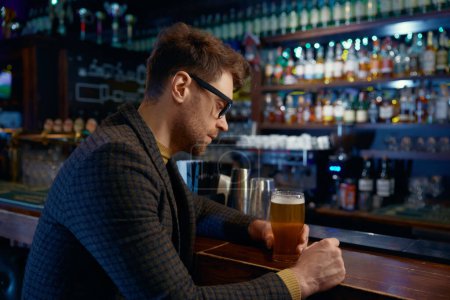 Téléchargez les photos : Pensif détendu souriant homme d'affaires tenant un verre de bière mousseuse froide dans le bar. Repos après le travail pendant, concept vendredi soir - en image libre de droit