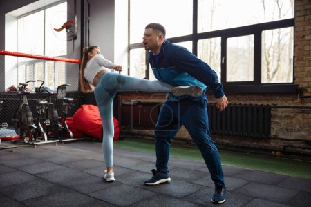 Téléchargez les photos : Jeune femme apprenant à se battre avec un entraîneur masculin dans la salle de gym fitness. Concept de fitness, de motivation, de sport et d'autonomisation des femmes - en image libre de droit