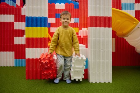 Téléchargez les photos : Enfant jouant avec d'énormes blocs de construction dans le centre de divertissement. Sécurité doux chantier coloré pour les enfants à la garderie aire de jeux - en image libre de droit