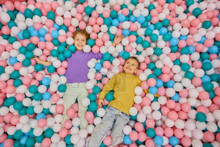 Téléchargez les photos : Heureux enfants enchantés couchés dans une immense piscine sèche avec des boules en plastique colorées vue aérienne. Vacances de fête d'enfants au centre de loisirs intérieur - en image libre de droit