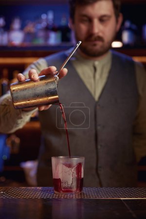 Téléchargez les photos : Élégant barman sérieux verser le sirop de la tasse de mélange dans le verre. Barman professionnel utilisant un équipement de bar pour préparer un cocktail alcoolisé et non alcoolisé - en image libre de droit