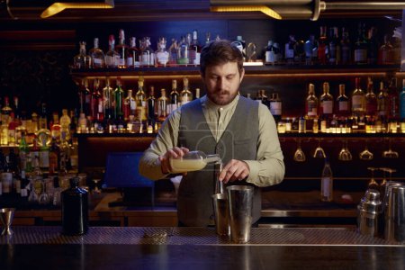 Téléchargez les photos : Un barman confiant qui boude de l'alcool pour faire un cocktail debout derrière le comptoir. Service professionnel et concept de profession - en image libre de droit