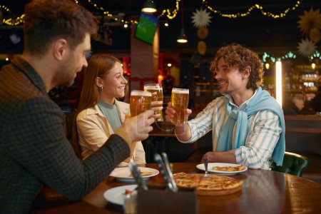 Photo for Group of friends football fans rest in sport bar celebrating victory of favorite soccer team. Young people feeling satisfaction drinking beer clinking glasses for success - Royalty Free Image