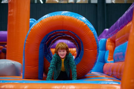 Téléchargez les photos : Garçon mignon jouant sur la maison gonflable de rebond dans le centre de divertissement. Fun et joie à l'aire de jeux intérieure - en image libre de droit