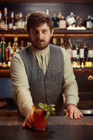 Téléchargez les photos : Portrait de barman donnant un cocktail au client d'une boîte de nuit ou d'un bar de l'hôtel. Barman professionnel offrant des boissons alcoolisées ou non alcoolisées, service visiteur faisant preuve d'hospitalité - en image libre de droit