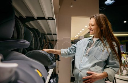 Photo for Happy pregnant woman buyer choosing comfortable and safety car seat for newborn in shopping mall. Purchases during pregnancy - Royalty Free Image