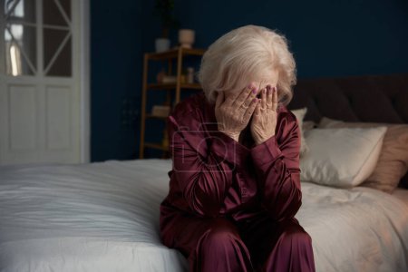 Foto de Mujer anciana triste infeliz usando pijamas sentados en la cama sintiendo soledad teniendo problemas psicológicos y mentales - Imagen libre de derechos