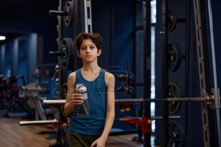Photo for Tired preteen boy with bottle of water having rest enjoying break time after training session at gym - Royalty Free Image