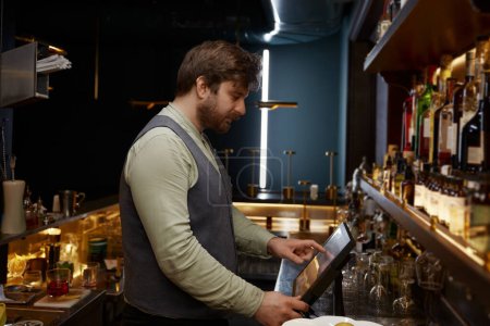 Bartender using digital panel to for processing bar visitors orders. Modern quick service at nightclub restaurant or pub