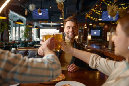 Foto de Gente feliz bebiendo cerveza mientras descansan en el pub. Hombre y mujer pareja reunión viejo amigo masculino sentado a la mesa teniendo conversación divertida, compartir momentos interesantes de la vida - Imagen libre de derechos