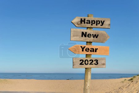 2023 happy new year written on a direction sign in front of a beach on blue sky 