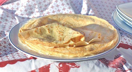 Téléchargez les photos : Crêpe artisanale traditionnelle française dans une assiette sur une nappe rouge et blanche - en image libre de droit