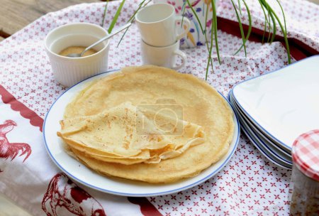 Téléchargez les photos : Crêpes maison traditionnelles françaises dans une assiette servie sur une table avec nappe rouge et blanche - en image libre de droit