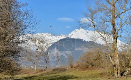 Foto de Hermoso paisaje escénico en la montaña alpina nevado y árboles en un prado con parapente lejos en el cielo - Imagen libre de derechos