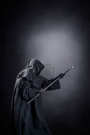 Photo for Wizard with hooded cape and magic staff over dark misty background - Royalty Free Image