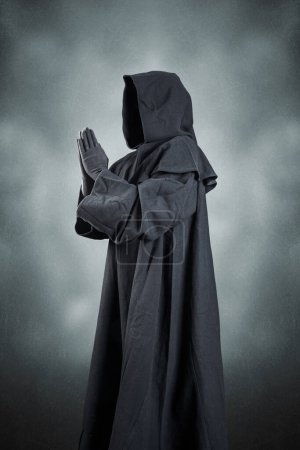 Foto de Monje medieval en capa encapuchada rezando en la oscuridad - Imagen libre de derechos