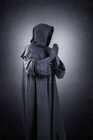 Foto de Monje medieval en capa encapuchada rezando en la oscuridad - Imagen libre de derechos
