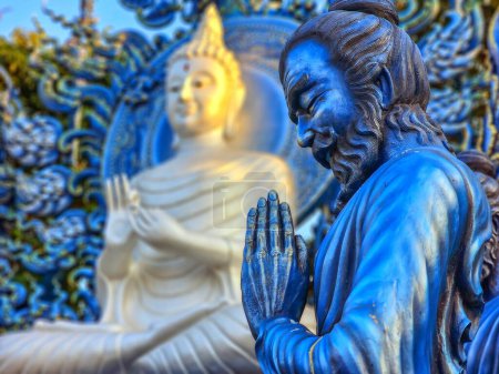 Téléchargez les photos : Statue de moine priant à côté de Bouddha au temple bleu de Wat Rong Suea Ten, Chiang Rai, Thaïlande - en image libre de droit