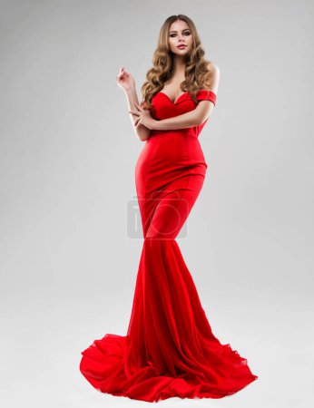Foto de Hermosa modelo en vestido largo rojo. Mujer de moda en vestido de sirena de noche sobre blanco. Glamour Girl con peinado ondulado rizado y maquillaje suave. Mujer Luxury Ropa - Imagen libre de derechos
