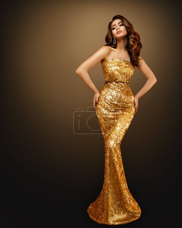 Modefrau im goldenen Paillettenkleid. Glamour Model in Goldglitzerkleid mit welliger Frisur vor dunklem Hintergrund. Elegante Dame im langen Abendkleid