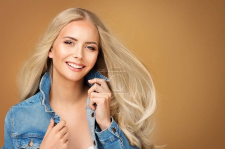 Photo for Happy Fashion Girl with Long Blond Hair. Beautiful Smiling Young Woman in Denim Jeans Jacket over Beige Background. Cheerful Model with Natural Make up and Summer Hairstyle - Royalty Free Image