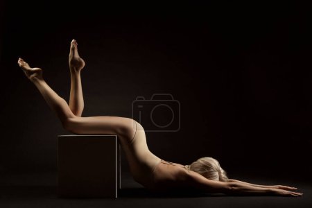 Téléchargez les photos : Silhouette sexy de corps de femme sur noir. Femme sensuelle s'étendant sur le cube. Belle Fit Girl Body Vue latérale faisant de l'exercice de yoga - en image libre de droit