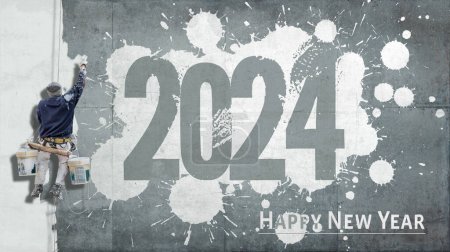 Photo for Building painter hanging from harness painting a industrial wall with the words happy new year 2024 - Royalty Free Image